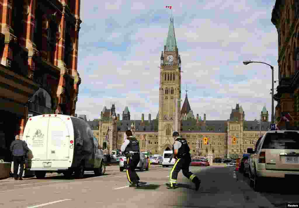 Armed RCMP officers race across a street on Parliament Hilll following a shooting incident in Ottawa.